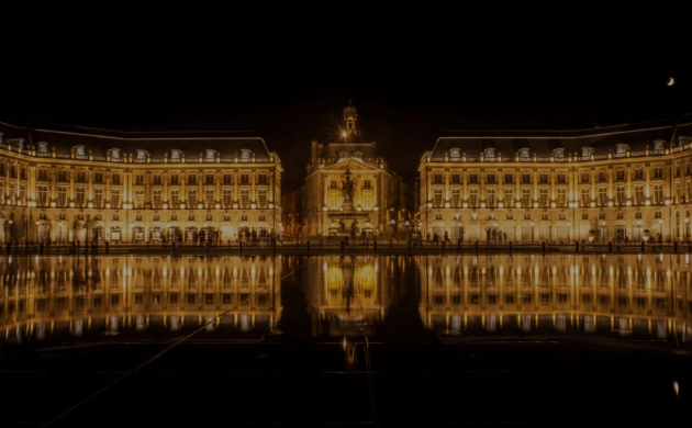 La Place de la Bourse à Bordeaux illuminée la nuit, se reflétant dans le Miroir d’eau emblématique du centre historique.