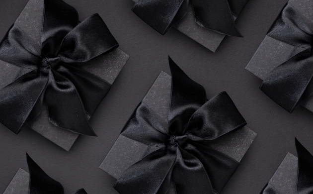 boîtes cadeau noires décorées d’un grand ruban noir en satin, disposées sur un fond noir