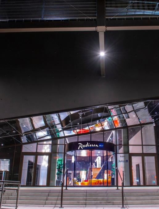 Entrée du Radisson Blu Bordeaux de nuit, avec une façade moderne et un jeu de reflets lumineux.