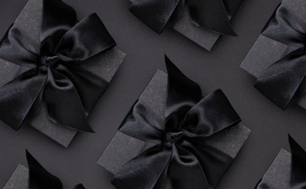 boîtes cadeau noires décorées d’un grand ruban noir en satin, disposées sur un fond noir
